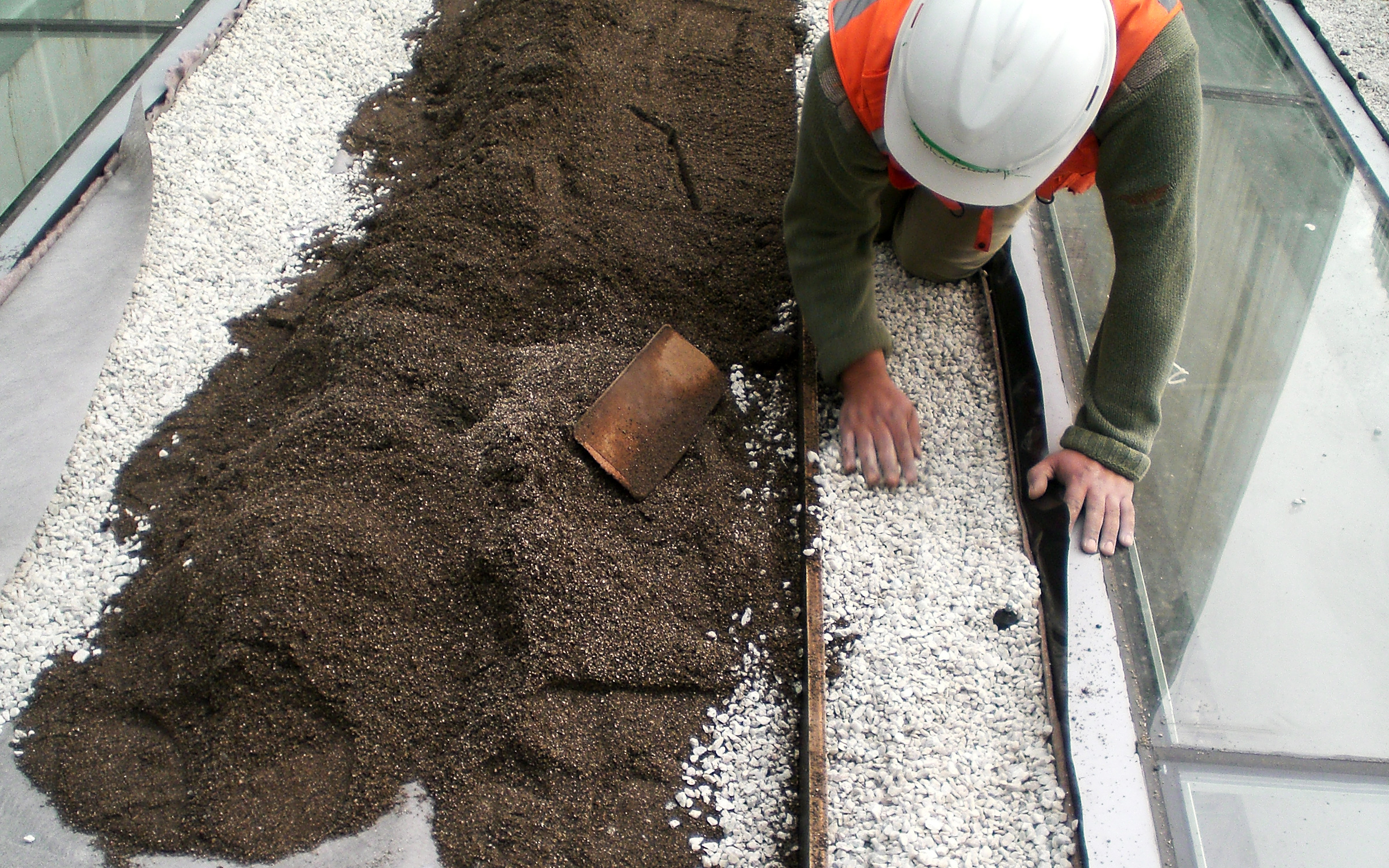 Worker distributing gravel and substrate on a rooftop